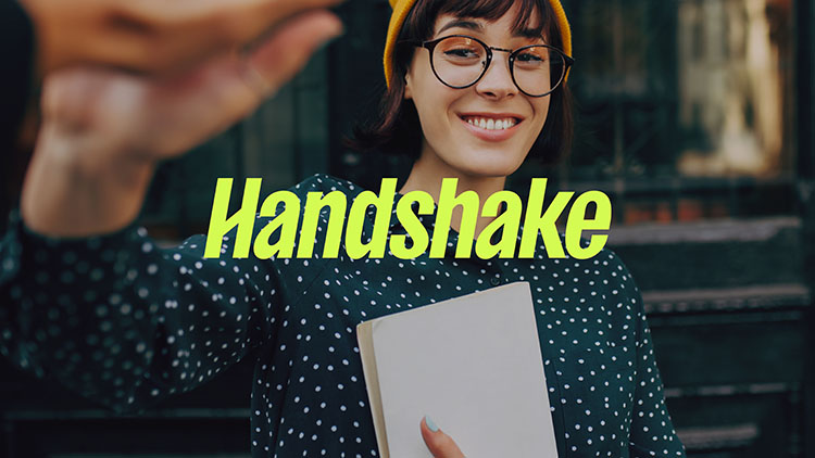 Person wearing yellow hat and holding a notebook with the word HANDSHAKE in yellow letters across the front of the image.