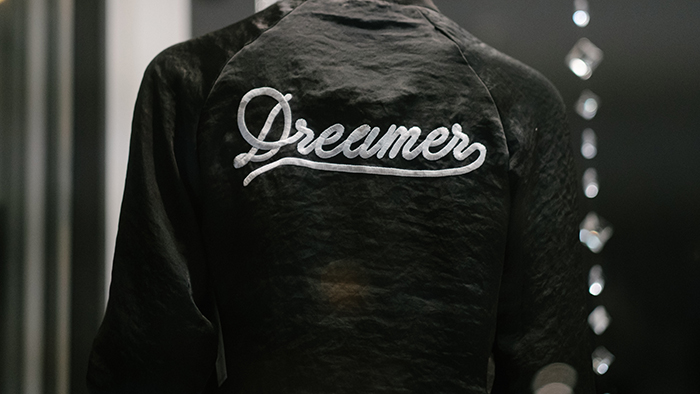 Black and white photo of a person wearing a jacket that has Dreamer embroidered on the back of it.