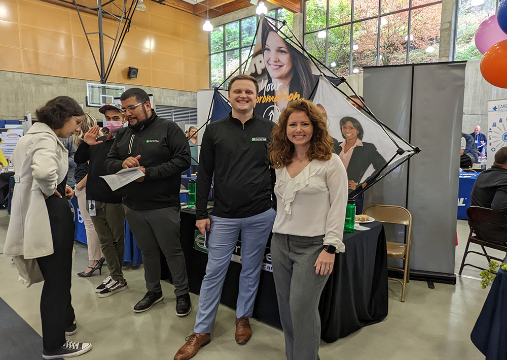 A couple standing in front of their booth smiling for the camera at an in-person career fair