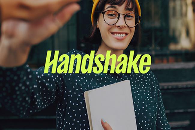yellow handshake logo (which is just the work handshake) over an image of a person wearing glasses, a yellow at and a polka dot shirt who is standing outside building.