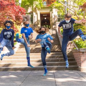 Four students wearing WWU t-shirts and jumping up in the air in front of Old Main